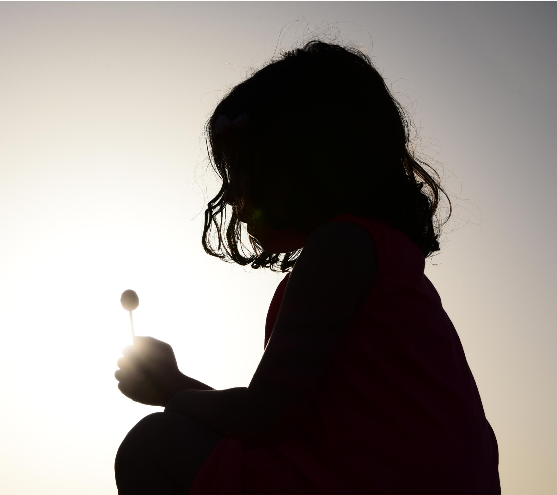 Silhouette of a young child holding a lollipop, symbolizing innocence, safety, and somatic calm through embodied healing.